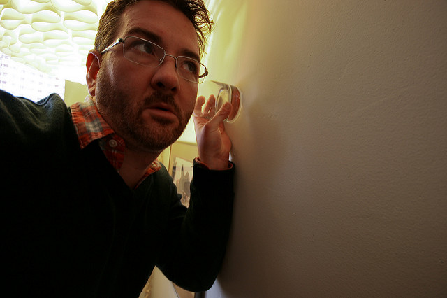 Man with a glass listening at a wall
