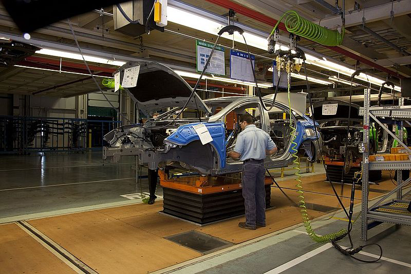A man is shown using a machine to install car parts on an assembly line.