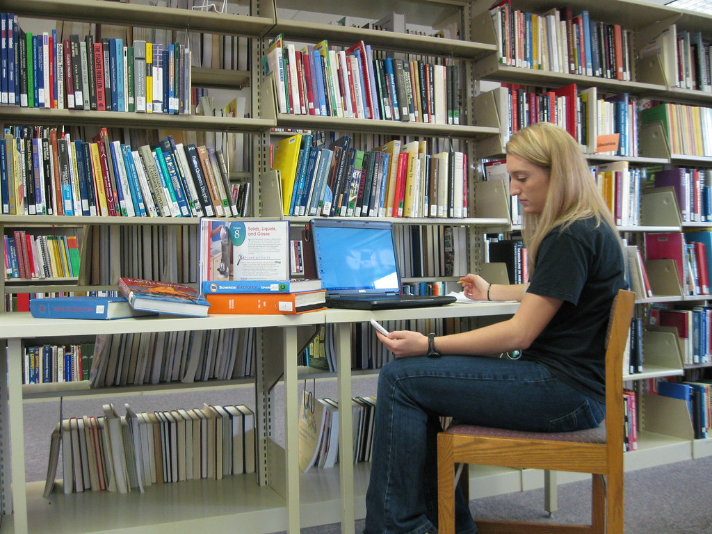Student studying in library glancing at phone