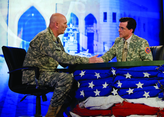 An image of Stephen Colbert and Ray Odierno seated on opposite sides of a table, facing each other.