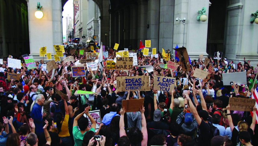 An image of a large crowd of people, several of whom are holding signs.